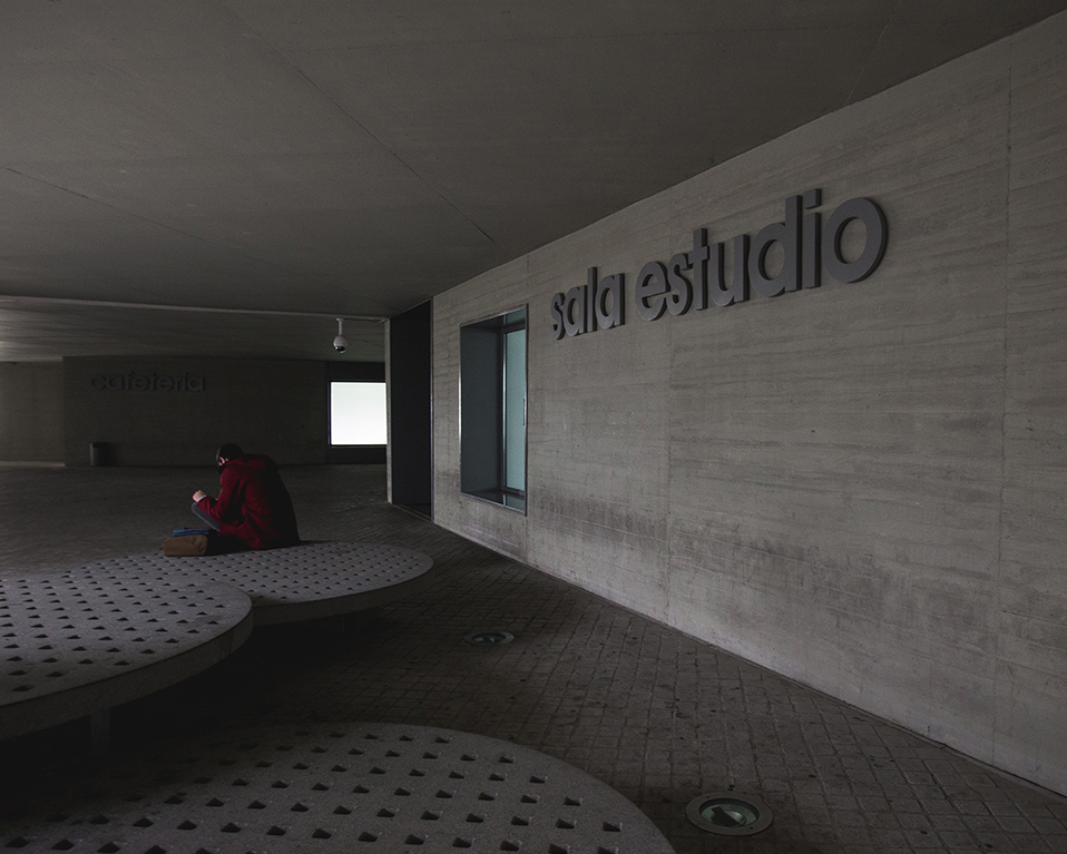 Vista exterior de la entrada a la sala de estudio situada en el Parque Tecnológico de la Salud. Hay bancos de estilo moderno en el que un estudiante permanece sentado